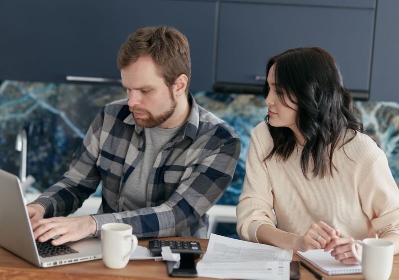 A couple working together on financial planning at home, using a laptop and paperwork.